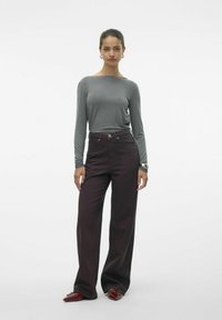 Top gris de manga larga combinado con pantalones burdeos de pierna ancha y cintura alta. Los accesorios incluyen pendientes de aro de plata y una pulsera gruesa.