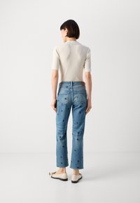 Lys beige ribbet topp med korte ermer, blå denim jeans med spredte mørkeblå prikker, og beige leiligheter med svarte såler.