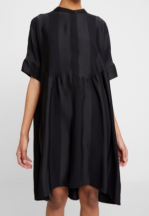 Schwarzes Kleid mit hohem Kragen, kurzen Ärmeln und lockerem Schnitt. Das Material hat vertikale Streifen und eine geraffte Taillendetail.