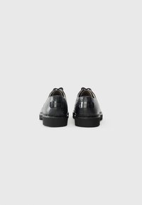 Pantofi din piele neagră cu un finisaj texturat, în relief de crocodil. Vârf rotund, toc mic și închidere decorativă cu șireturi. Detaliu subtil cu eticheta brandului.