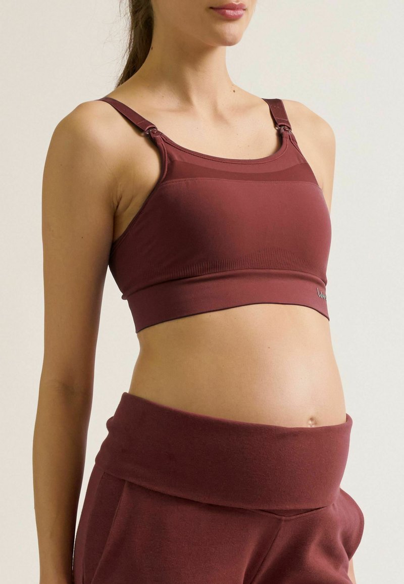 Soutien-gorge de maternité bordeaux avec une texture lisse, des straps réglables et une large bande. Associe avec un pantalon taille haute assorti.