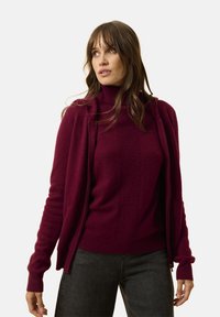 Bordowy sweter typu golf z teksturowanym wzorem, noszony pod dopasowanym kardiganem z otwartym przodem; miękka tkanina, prążkowane mankiety i dół.