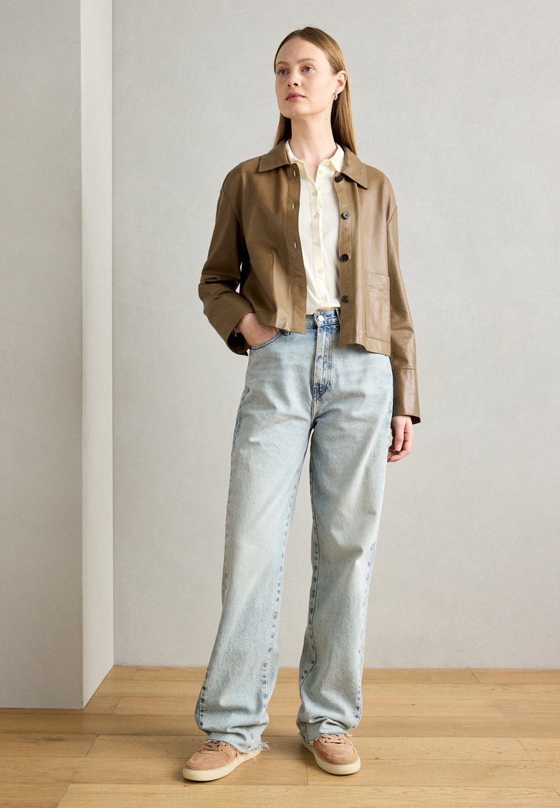 Giacca cropped in pelle marrone, camicia leggera con bottoni, jeans in denim azzurro chiaro a vita alta e sneakers beige. Design semplice e casual.
