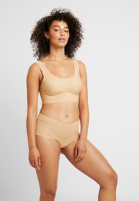 Conjunto de sujetador sin costuras en color beige y braguitas de cintura alta, con tejido suave y tirantes anchos para mayor comodidad. Diseño simple y funcional.
