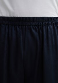 Pantalons bleu marine avec une taille  élastique, au toucher lisse et à motif géométrique subtil. Plis de tissu visibles au niveau de la taille.
