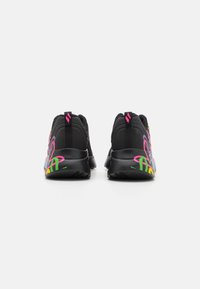 Scarpe da ginnastica nere con vivaci design in graffiti neon sui talloni, con linguette visibili e logo rosa, mostrate da dietro su sfondo bianco.