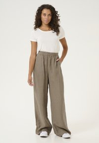Wide-leg trousers in textured tan fabric, featuring an elastic waistband and side pockets. Paired with a plain white short-sleeve top.