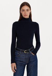 Top de gola alta em malha canelada navy com mangas longas, combinado com jeans escuros de cintura alta e um cinto preto com fivela dourada.