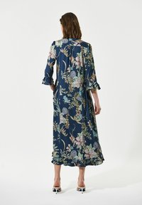 Maxikleid aus marineblauem Stoff mit Rüschenärmel und Saum, das mehrfarbige botanische Drucke zeigt. A-Linien-Silhouette mit lockerem Sitz.