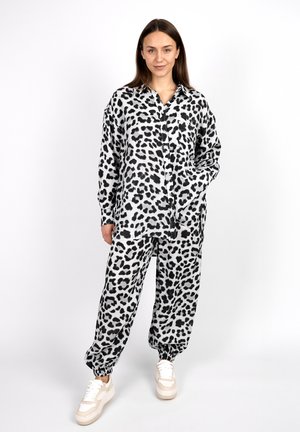 Schwarz-weißes Loungewear-Set mit Leopardenmuster, bestehend aus einem lockeren, knöpfbaren Oberteil und elastischen, umgekrempelten Hosen, kombiniert mit klobigen Turnschuhen.
