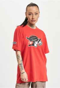 Rød bomull T-skjorte med et svart og hvitt grafisk design som viser en hatt og et kors. Løs passform med korte ermer og et merke på ermene.