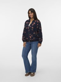 Floral bomber jacket in navy with pink accents, zip closure, loose fit, and ribbed cuffs. Paired with blue flared jeans and brown shoes.