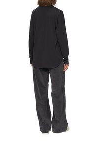 Zwart langmouwen shirt met een ronde hals, gecombineerd met grijze corduroy wijde broek en witte sneakers, gezien vanuit de rug.