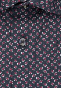 Camicia blu navy con una piccola stampa floreale in rosa e bianco, dotata di chiusura con bottoni e tessuto testurizzato.