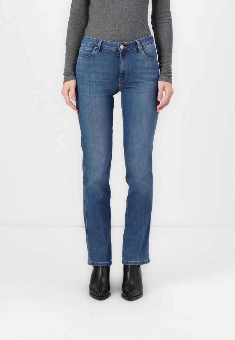 Blugi din denim de culoare albastră închisă cu un design drept, având talie medie și buzunare frontale, asociați cu cizme negre până la gleznă.