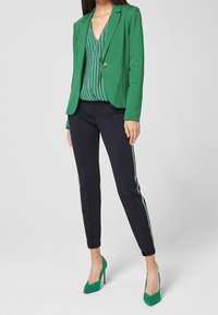 Zielony blezer na paski, zielona i biała bluzka, w połączeniu z granatowymi spodniami z bocznymi paskami. Zielone szpilki dopełniają strój.