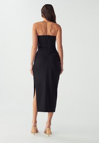 Schwarzes, trägerloses Midikleid mit engem Oberteil, seitlichem Schlitz und eleganter Silhouette. Glattes Material mit einem verdeckten Reißverschluss auf der Rückseite.