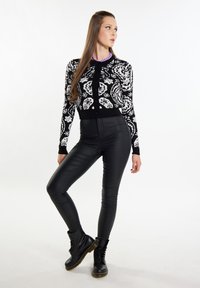 Cardigan a motivi in bianco e nero con maniche lunghe, chiusura con bottoni, abbinato a pantaloni neri in ecopelle a vita alta e stivali neri con lacci.
