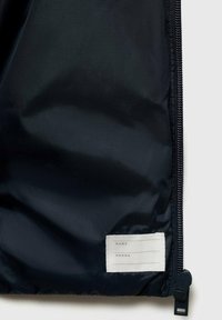 Borsa in nylon blu navy con una texture liscia, dotata di una zip e di un'etichetta bianca per informazioni personali con righe per nome e telefono.
