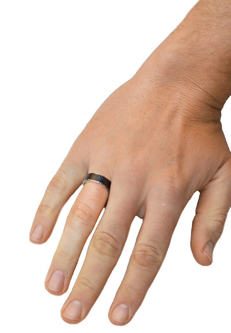 Schwarzer und silberner Bandring an einer Hand mit heller Haut; der Ring hat eine strukturierte Oberfläche, glatt polierte Kanten und eine abgerundete Form.