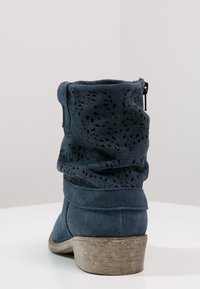Niebieski zamszowy botek za kostkę o luźnej konstrukcji, z perforowaną cholewką i niskim, teksturowanym beżowym obcasem. Zamek błyskawiczny po boku zapewniający zapięcie.