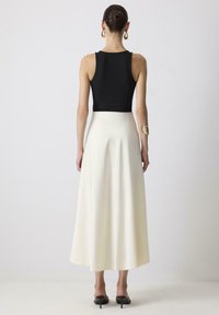 Zwarte aansluitende tanktop gecombineerd met een crèmekleurige, middelange rok. Glad textuur, uitlopende stijl en zwarte hoge hak sandalen met achterkant straps.