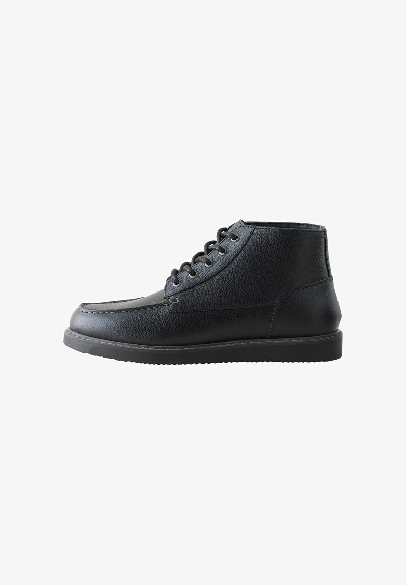 Bottine en cuir noir avec un laçage à l'avant, couture moc toe et semelle en caoutchouc plate, présentée en profil latéral.