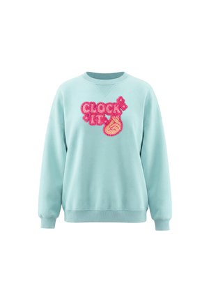 Lyseblå sweatshirt med lyserød, fluffy tekst "CLOCK IT" og en hånd, der laver en knipsereflektsion foran.