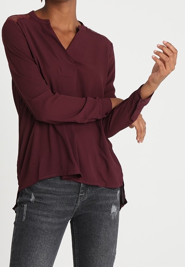 Blusa bordeaux realizzata in tessuto leggero, con scollatura a V, maniche lunghe e dettagli in pizzo sulle spalle. Abbinata a jeans neri strappati.
