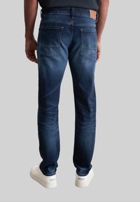 Donkerblauwe denim jeans met een rechte snit, voorzien van twee achterzakken en een tan leren patch op de tailleband.