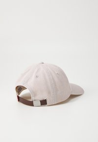 Light beige cotton cap with a curved brim, rear strap adjustment in brown, and contrasting gray stitching, featuring a small logo tag.