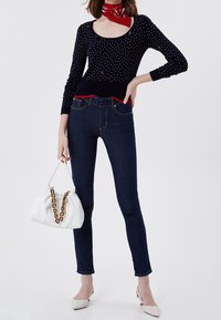 Pull marine à pois, manches longues, encolure dégagée ; jean skinny en denim foncé ; sac à main blanc avec bandoulière chaîne ; escarpins blancs pointus.