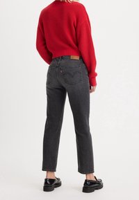 Vaqueros negros de corte recto, cintura alta y sutiles bolsillos traseros. Combinados con un suéter de punto rojo y zapatos negros.