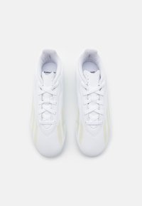 Zapatillas deportivas blancas con un material sintético suave, presentan cordones blancos y sutiles rayas amarillas en los laterales; diseño de punta redondeada.