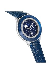 Niebieski skórzany pasek o teksturze krokodylej, srebrny zegarek, niebieska luneta oraz tarcza przedstawiająca gwiezdną noc z akcentami kryształowymi i unikalnym wzorem księżyca.