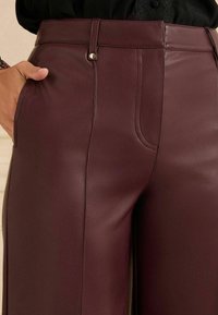 Burgunderrote Lederhosen mit hoher Taille, Fronttaschen und glatter Textur. Verfügt über einen einzelnen goldenen Knopf am Bund.