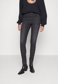 Jeans negros ajustados con una textura desgastada, cinturilla alta y diseño de cinco bolsillos, emparejados con botas negras hasta el tobillo y un sudadera negra.