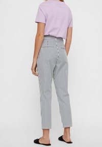 Pantalon rayé à jambe fuselée en noir et blanc, avec une taille haute, des poches arrière et une texture de tissu lisse.