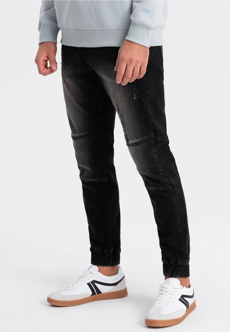 Svart denim joggers med slim fit, med slitna detaljer, ribbad fotled och sömmar på frontpanelen. Kombinerat med vita sneakers.