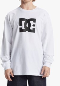 White long-sleeve t-shirt featuring a large black DC logo and star on the front. Made of cotton, it has a loose fit and ribbed cuffs.