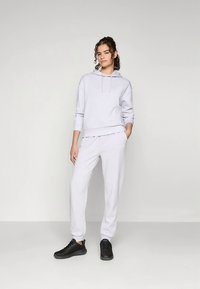 Gaiši pelēka kapuce ar regulējamiem aukliņām, kombinēta ar saskaņotām skriešanas biksēm. Piedāvā vaļīgu piegriezumu un ribas aproces, valkāta ar melnām sporta kurpēm.