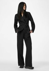 Costume noir à fines rayures comprenant un blazer ajusté avec un bouton unique et un pantalon à jambes larges. Tissu lisse avec une coupe sur mesure.