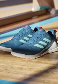 Scarpe da ginnastica blu con tre strisce verde chiaro, tomaia testurizzata, design con lacci e dettagli rossi sul tallone. Suola in gomma per trazione.