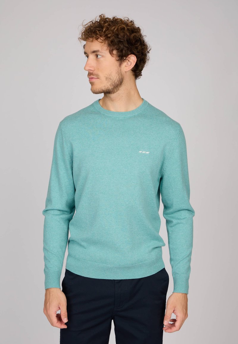 Pull en tricot turquoise clair, à manches longues, col rond et petit logo blanc sur la poitrine. Texture lisse et coupe décontractée.