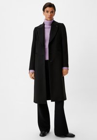 Schwarzer Wollmantel mit taillierter Passform, einreihiger Knopfverschluss und Reverskragen, kombiniert mit einem helllila Rollkragenpullover und schwarzen Hosen.