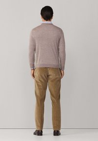 Svetlý hnedý sveter s okrúhlym výstrihom a dlhými rukávmi, spojený s krémovými kordúrovými nohavicami. Topánky sú tmavo hnedé.