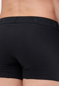 Sorte boxertruser med en glatt tekstur og en bred linning som har preget "SAMØE" merkevare. Enkel, tettsittende design uten ytterligere mønstre.