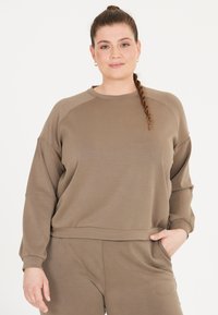 Brun sweatshirt med avslappnad passform, ribbade ärmslut och rundad halsringning, tillverkad av mjukt tyg. Matchas med koordinerande byxor.