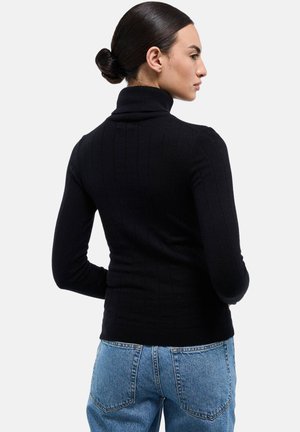 Pull noir côtelé à col roulé avec manches longues, doté d'une coupe ajustée. Porté avec un jean taille haute bleu clair, mettant en valeur une silhouette élégante.