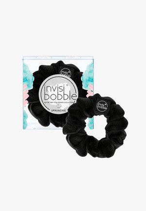 Zwarte Invisibobble scrunchie naast de doorzichtige doosverpakking met blauwe en roze accenten en zichtbaar merktekst.